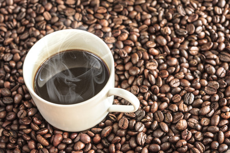 Hot coffee over coffee beans background with copy space, coffee cup on coffee beans backdrop close upの写真素材
