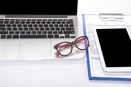 Doctors desk with computer notebook, tablet, glasses and patient history form on white table with copy spaceの写真素材