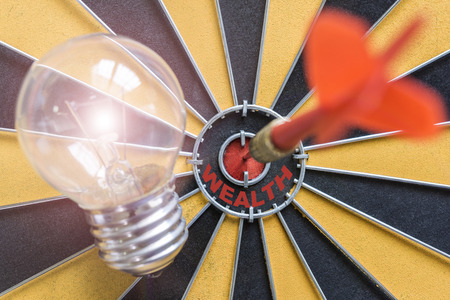 Arrow hitting the wealth bullseye target with idea lamp on dartboard, Success business finance wealth profit concept, symbol of successfulの写真素材