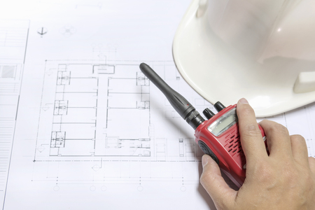 engineer hand holding radio communication on architectural blueprints paper near helmet, architect engineering and contractor conceptの写真素材