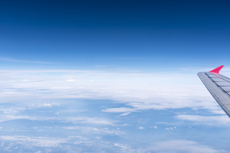 airplane wing out of window above blue sky with clouds, skyline view from aircraftの写真素材