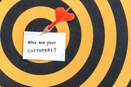 Target arrow hitting paper with alphabet letters of handwriting words who are your customers and question mark symbol over bullseye in dartboard, Target customers marketing conceptの写真素材