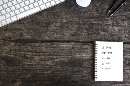 a goal without a plan is just a wish motivational handwriting on a notebook with mouse keyboard and pen over grungy tableの写真素材