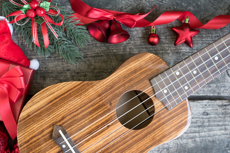 Ukulele on the wooden table with fir twigs and red christmas ornament decoration with gift box and santa claus hatの写真素材