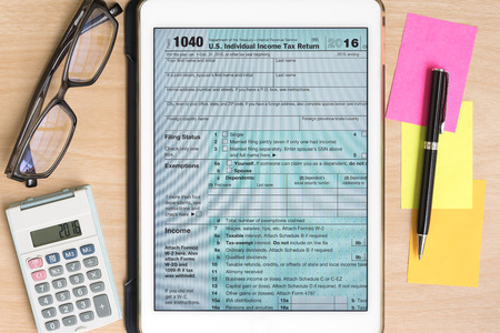 US Tax form 1040 in tablet with calculator and pen on sticky note on wooden deskの写真素材