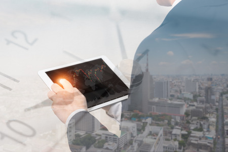 Double exposure of businessman using the tablet with cityscape and financial graph on blurred building background with time, Business Trading conceptの写真素材