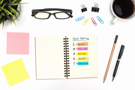 Smart goal setting on spiral notebook with pen, pencil, office supply, eye glasses and coffee cup over white desk table  background, Business success conceptの写真素材