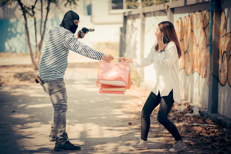 Street thief stealing young woman shopping bag and threatening with gun, Vintage tone styleの写真素材