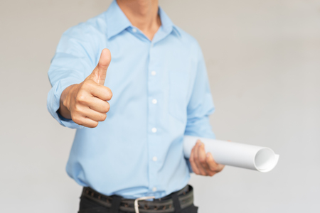 Engineer with blue shirt holding blueprint and thumb up over off white background with copy spaceの写真素材