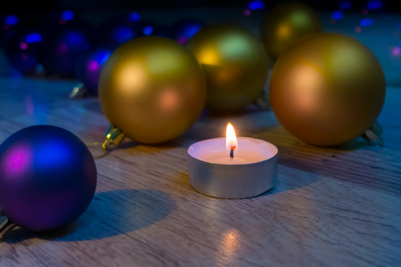 Golden and violet Christmas ball ornaments with a burning candle on the wooden background.の写真素材