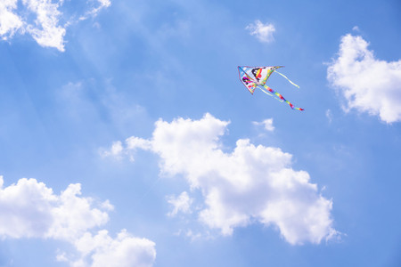 A carefree kite flying high in the blue summer sky with a few white clouds in the background.