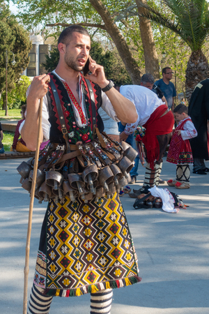 Varna, Bulgaria - April 28, 2018: Participants of the annual Varna Spring Carnival. Man in traditional kukeri costume with many bells attached to his belt talks on a mobile phone.のeditorial素材
