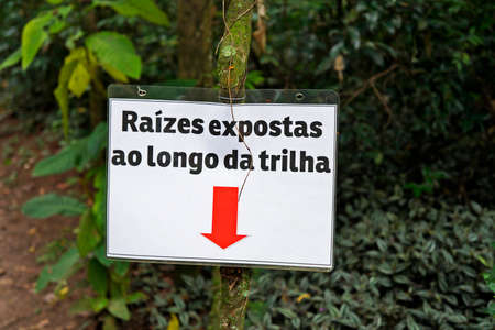 Rio de Janeiro, Brazil - December 21, 2019: Warning sign in portuguese that says: Roots exposed along the trail. "Bosque da Freguesia" Public park in the neighborhood of Jacarepagua.のeditorial素材