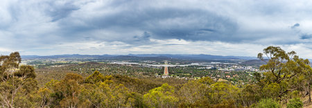 A wide view captures the lush landscape of Canberra, featuring the city skyline, Parliament House, and rolling hills beneath overcast skies.の写真素材
