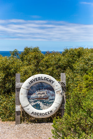 A coastal sign with lifebuoy stands in Anglesea on the Great Ocean Road among vibrant greenery against a clear blue sky, inviting visitors to explore the area.の写真素材