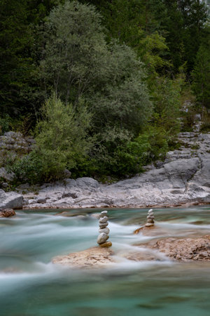 Scenic view of the turquoise Soca River with stacked rocks near Bovec, Slovenia. Lush green trees surround the fast-flowing water.の写真素材