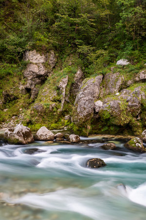 Soca river flows over rocks in Kobarid, Slovenia's natural landscape. The water moves softly among...