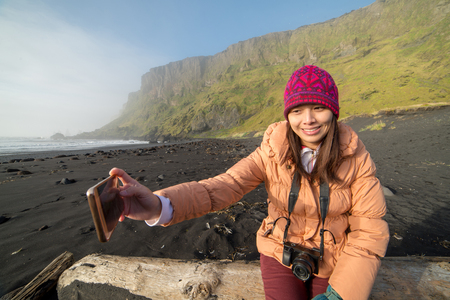 A women taking selfies by her smartphone at Black Sand Beack, Vik, Icelandの写真素材