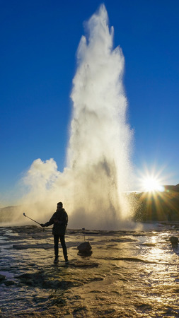 Male tourist took photo himself in between Geysir hot spring eruption.の写真素材