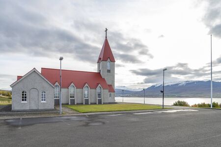 In the morning at chapel on small hill opposite Akureyri city. The Christian cross on roof top of chapel contrast with white sky waiting sunrise.の写真素材