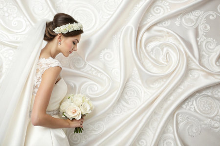 Two wedding rings presented on ornate white lace fabric.の素材