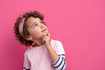 A charming little girl in beret looks up thoughtfully on a pink background.の素材