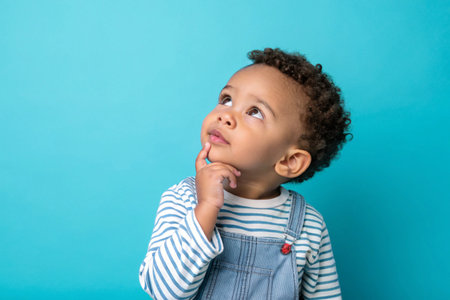 A young child in a yellow beanie thoughtfully gazes upward on blue background.の素材