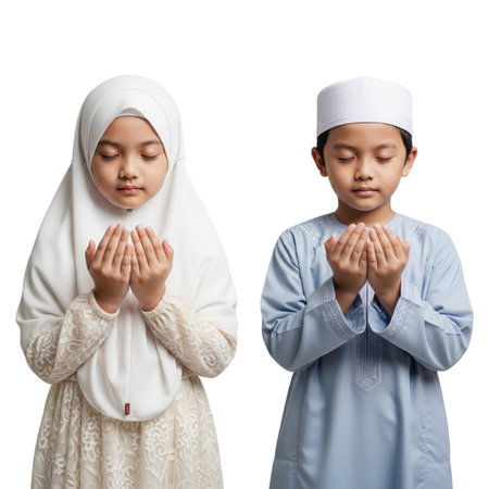 Two young Muslim children praying with closed eyes, hands raised, wearing traditional religious clothing against a black backgroundの素材