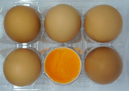 Brown eggs in carton box. Broken egg with yolk in background.