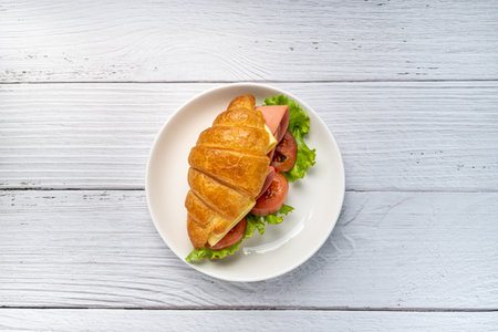 Fresh croissant sandwich with ham , cheese , tomato and salad leaf on white wooden background....