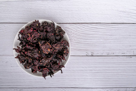 Dried Roselle flower buds in plate  on white wood background. In Traditional Chinese Medicine, Red roselle can make healthy beverage the source of Vitamin.の写真素材