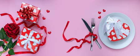Romantic dinner table. Gift or present box, red rose, mini heart, plate, fork and knives with ribbon...