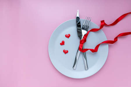 Romantic dinner table. plate, fork and knives with ribbon on pink background. for banner. The concept of Valentine Day. top view, copy spaceの写真素材