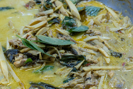 Delicious curry being prepared with chicken, herbs, and spices in a bustling kitchen during evening cooking sessionの写真素材