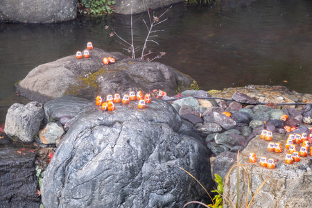 Orange figures are arranged on large rocks by a stream. The scene shows a mix of smooth stones and flowing water, creating a simple outdoor setting during the day.の写真素材