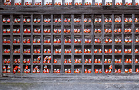 Small dolls line a wooden shelf in a building. Each doll has a painted face and bright colors. The scene shows a cultural display during daytime hours.の写真素材