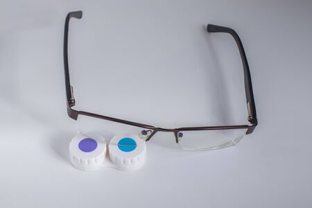 Contact lenses in a case and glasses on a white background
