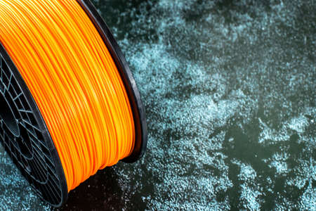 Filament for 3d printing. Bright thermoplastic of neon orange, color. Reel vertical view. Macro