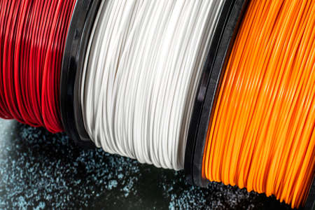 Three coils of filament for 3d printing. Bright thermoplastic of red, white smd orange colors. Reels vertical view.の写真素材