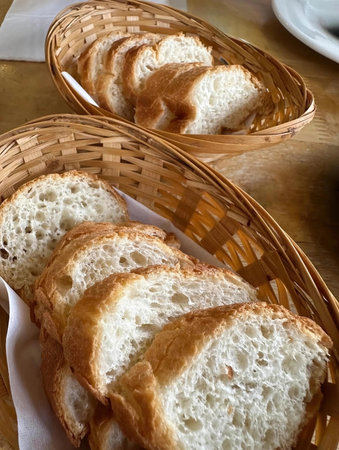 Freshly sliced crusty white bread in woven baskets. Soft on the inside, golden on the...