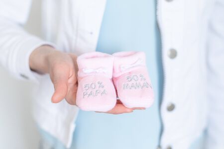 young pregnant woman with baby booties in hands - 50% Dad 50% Mum - Gender reveal 