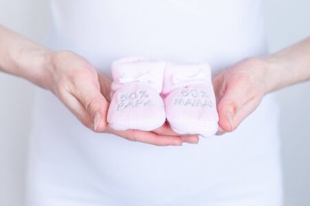 young pregnant woman with baby booties in hands - 50% Dad 50% Mum - Gender reveal