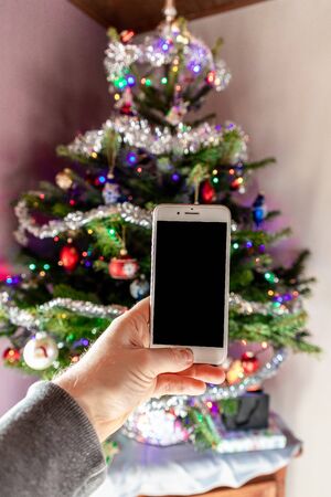 Mockup image of a man's hand holding black mobile phone with black screen with christmas backgroundの写真素材