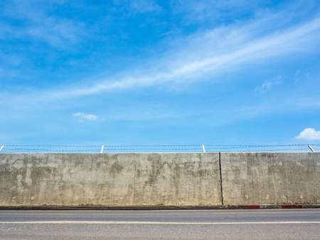 Concrete wall street with barbed wire fence under a blue sky and clouds background.For design with copy space for text or image.の写真素材