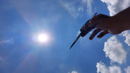 hand of artist with a paintbrush against the blue sky with cloudsの写真素材