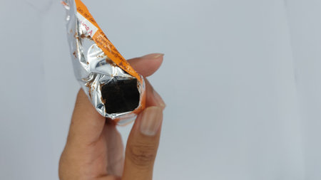 Woman hand holding a piece of chocolate in plastic bag on white backgroundの写真素材