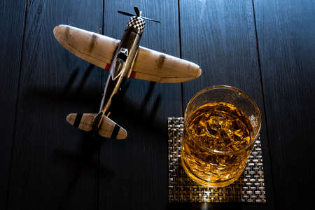 Airplane model and whiskey in a glass with ice on a wooden tableの写真素材