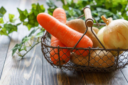 Raw unpeeled potatoes, onions and carrots on the wooden tableの写真素材