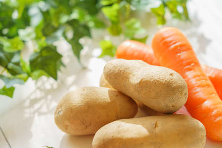 Raw unpeeled potatoes and carrots on the wooden tableの写真素材