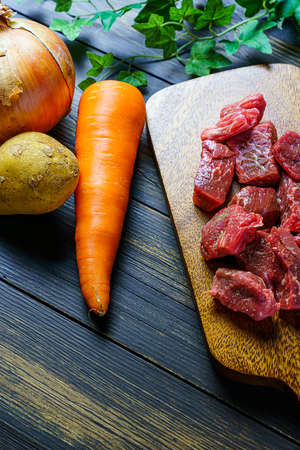 Raw unpeeled potatoes, onions, carrots, and beef on the wooden table